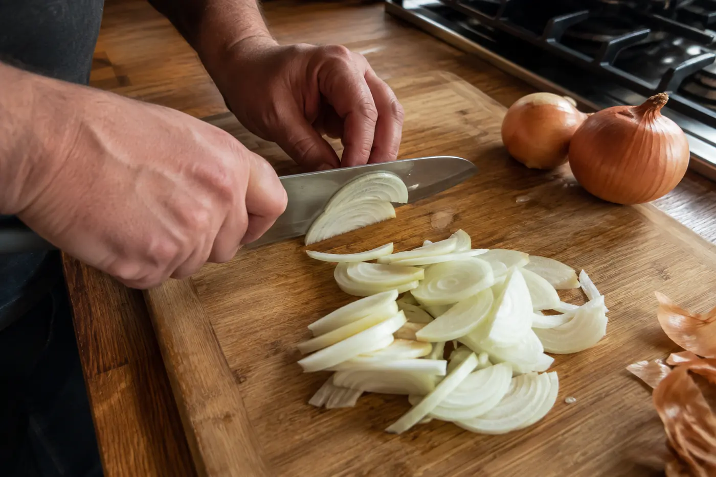 Thinly slicing yellow onions on a wooden cutting board for French onion soup