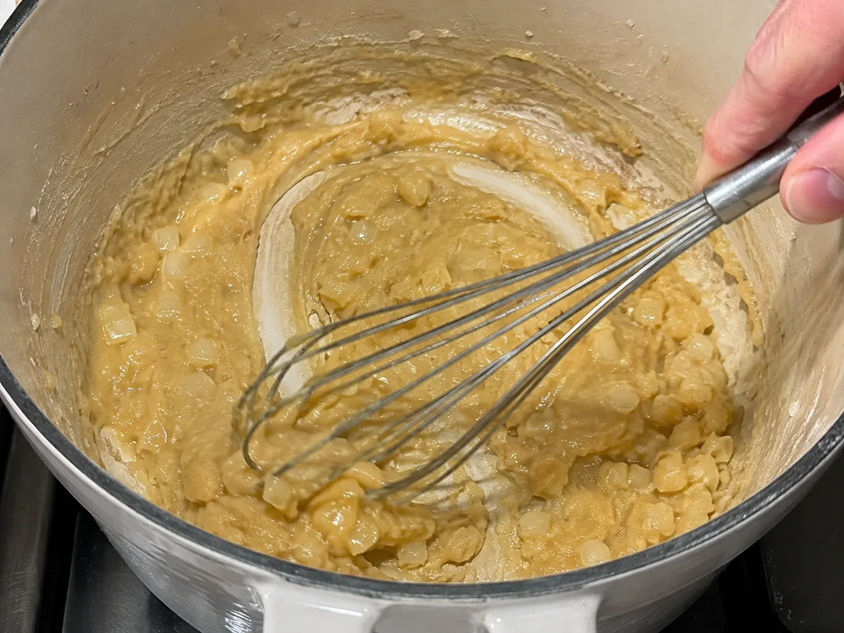 Flour being whisked into butter and onion to make a pale roux for broccoli cheddar soup.