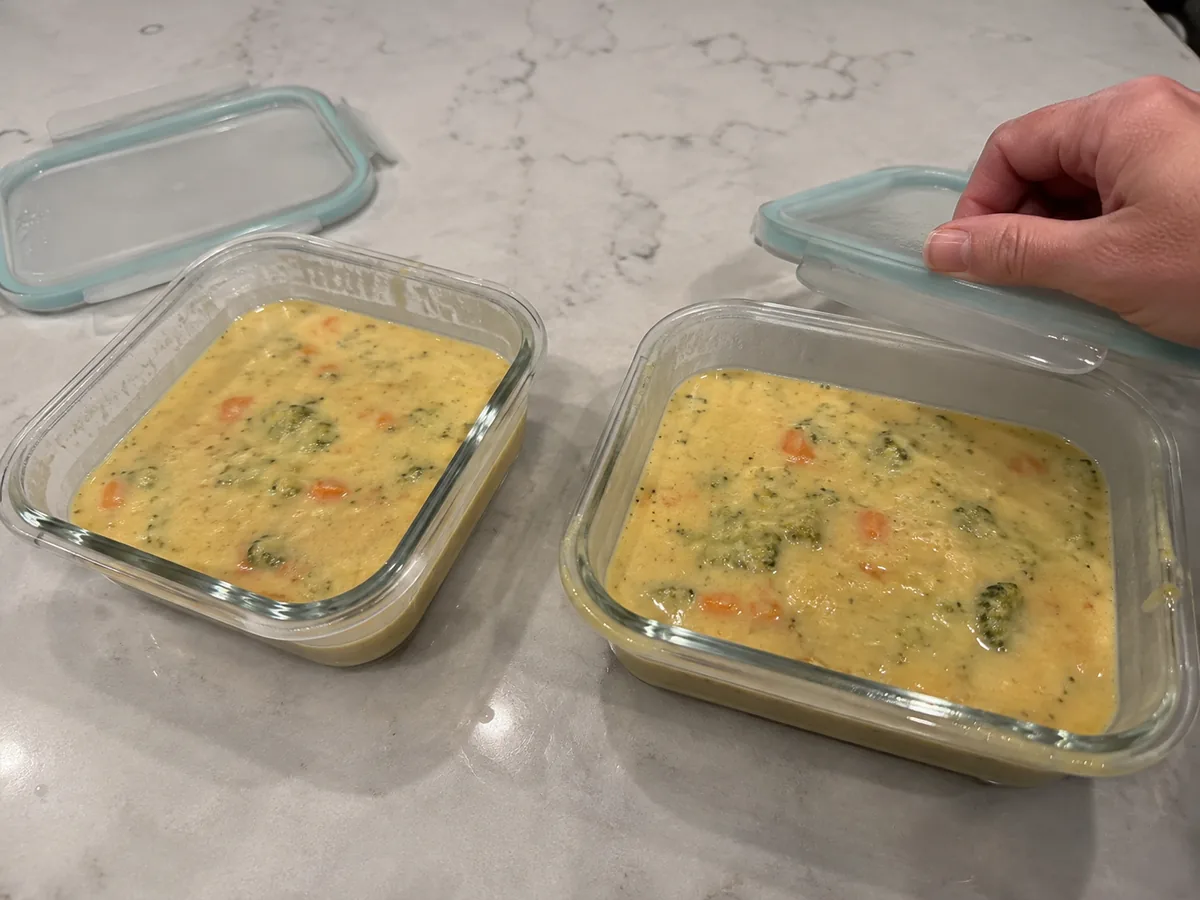 Broccoli cheddar soup divided into shallow glass containers for refrigerator storage.