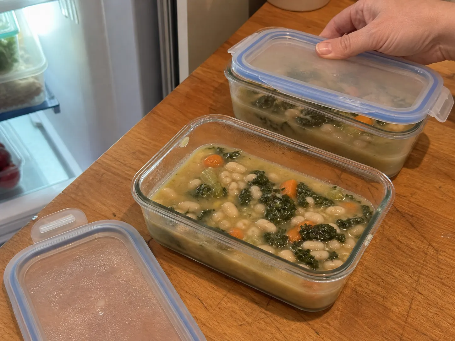 White bean and kale soup divided into shallow covered containers for refrigerator storage.